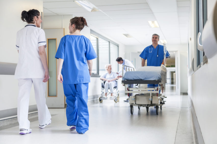 Male nurse pushing stretcher gurney bed in hospital corridor with doctors and senior female patient